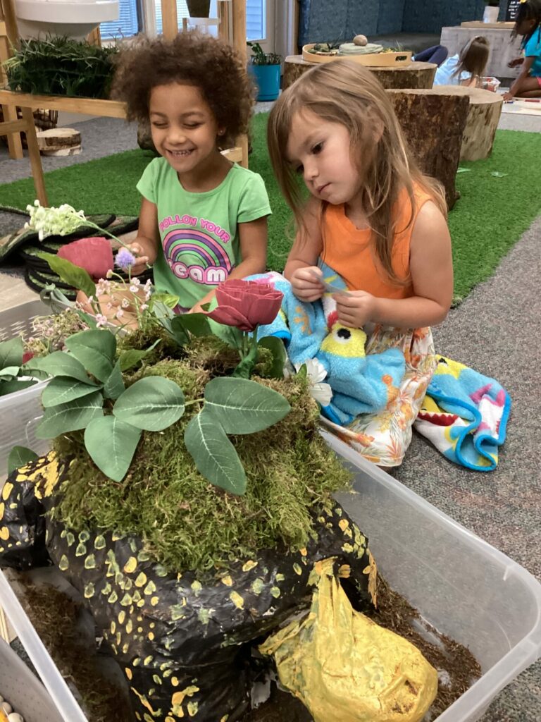 Two girls observing plants and flowers in a container.