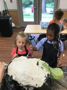 Two children making a paper mache turtle